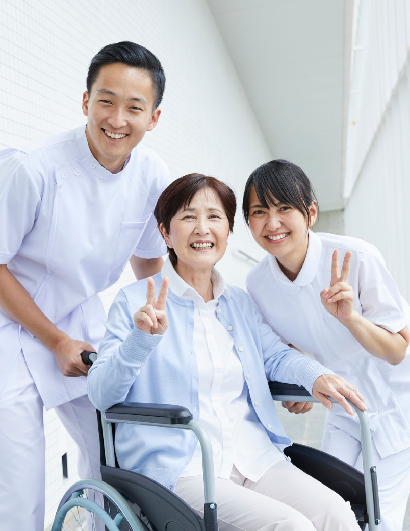 Smiling elderly woman in wheelchair with two dental professionals, promoting compassionate care and patient comfort at Ashar Dentistry.