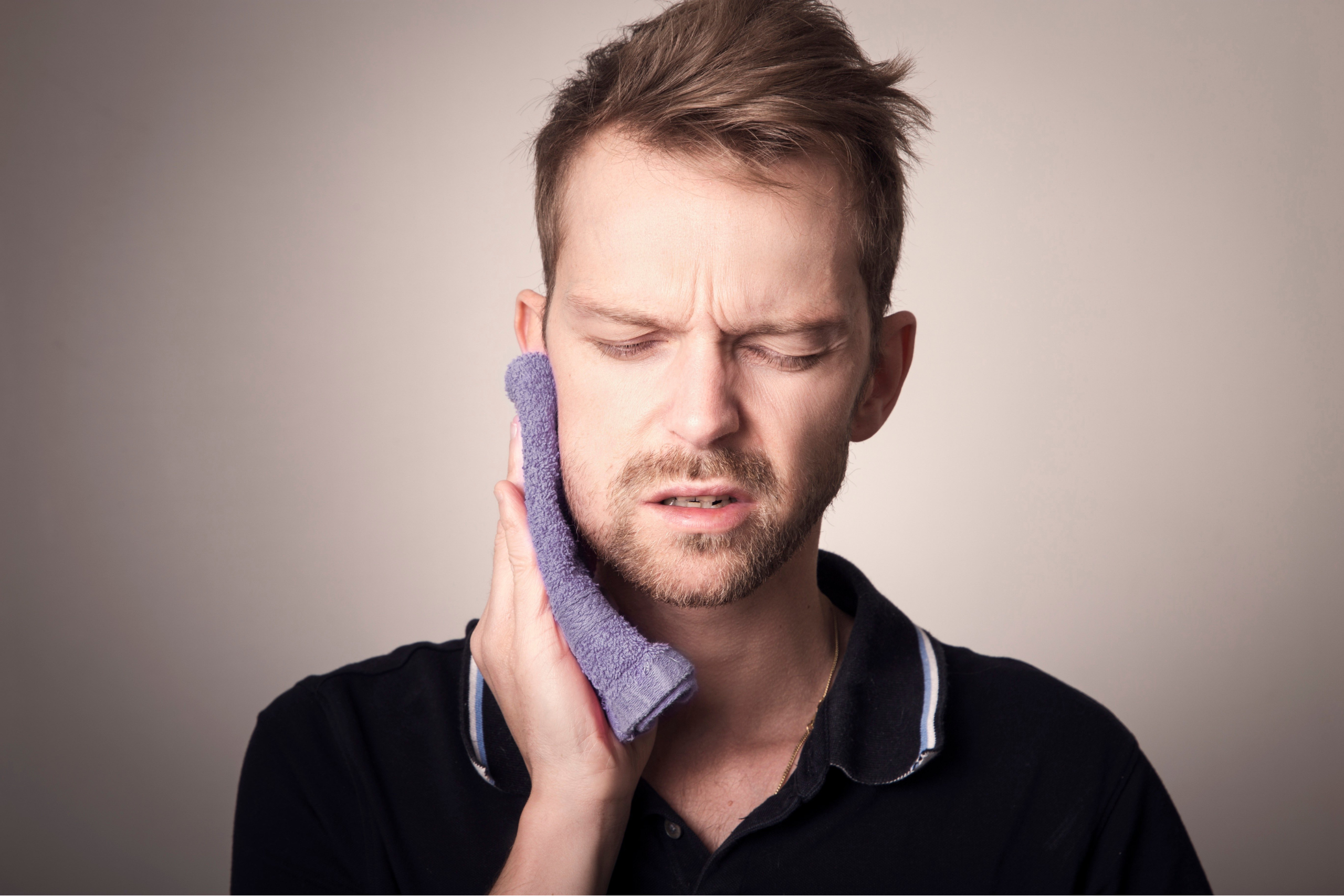 Man holding a towel to his jaw, expressing discomfort related to dental pain, highlighting the need for tooth extraction services.