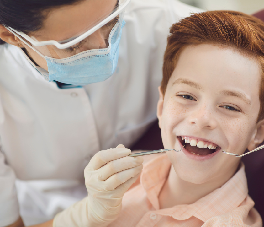 Child smiling in dental chair during check-up with dentist in mask and gloves, showcasing a positive dental experience at Ashar Dentistry.