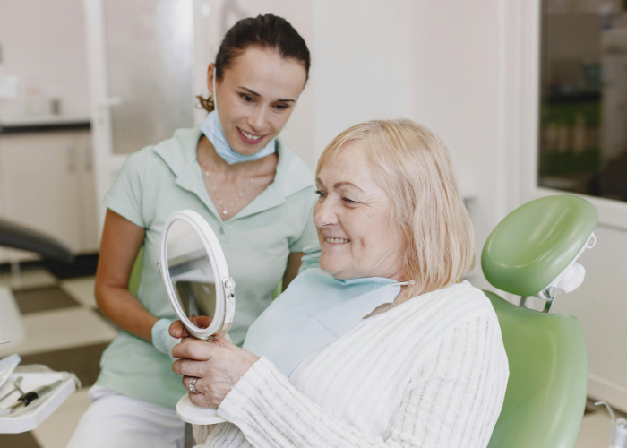 Dental patient smiling while holding a mirror, with a dental professional assisting in a modern clinic setting, highlighting patient care and satisfaction after dental implant procedure.